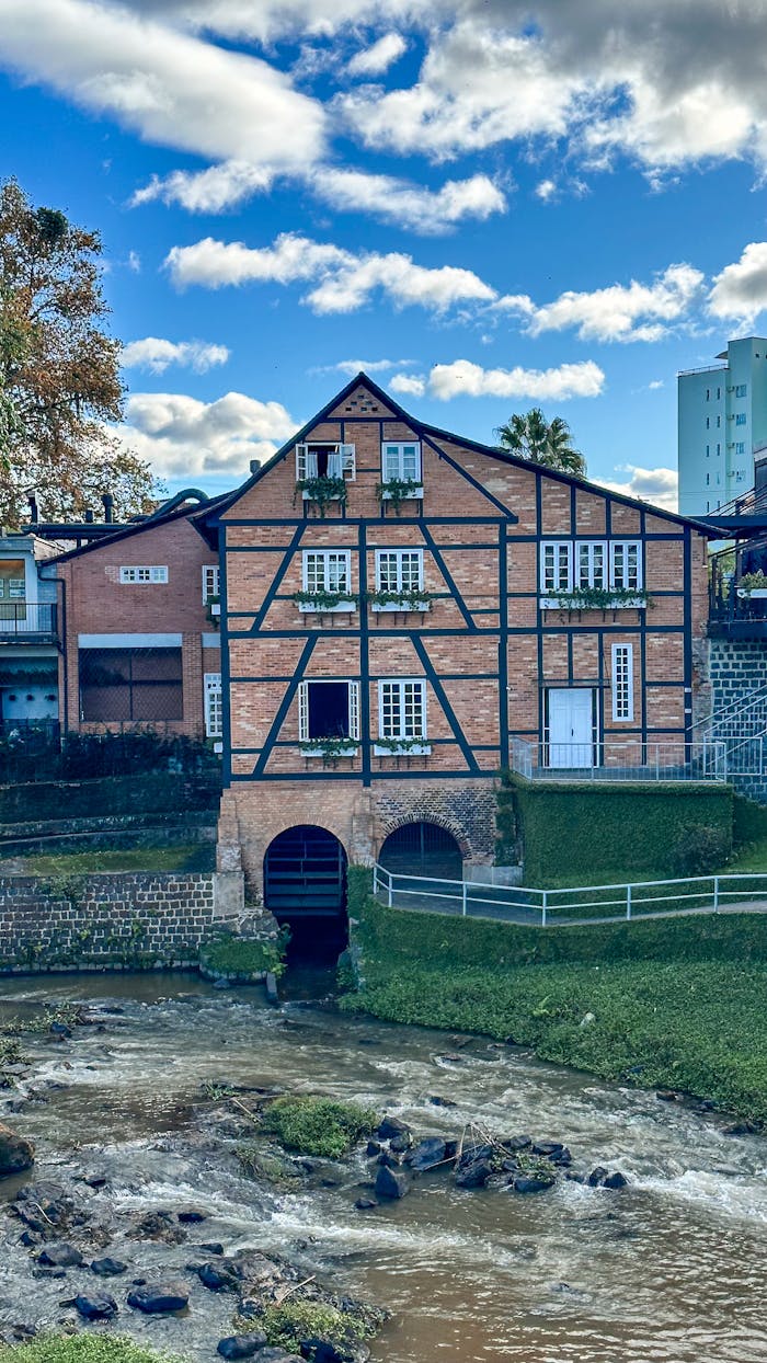 A picturesque half-timbered house by a flowing river under a vibrant blue sky.